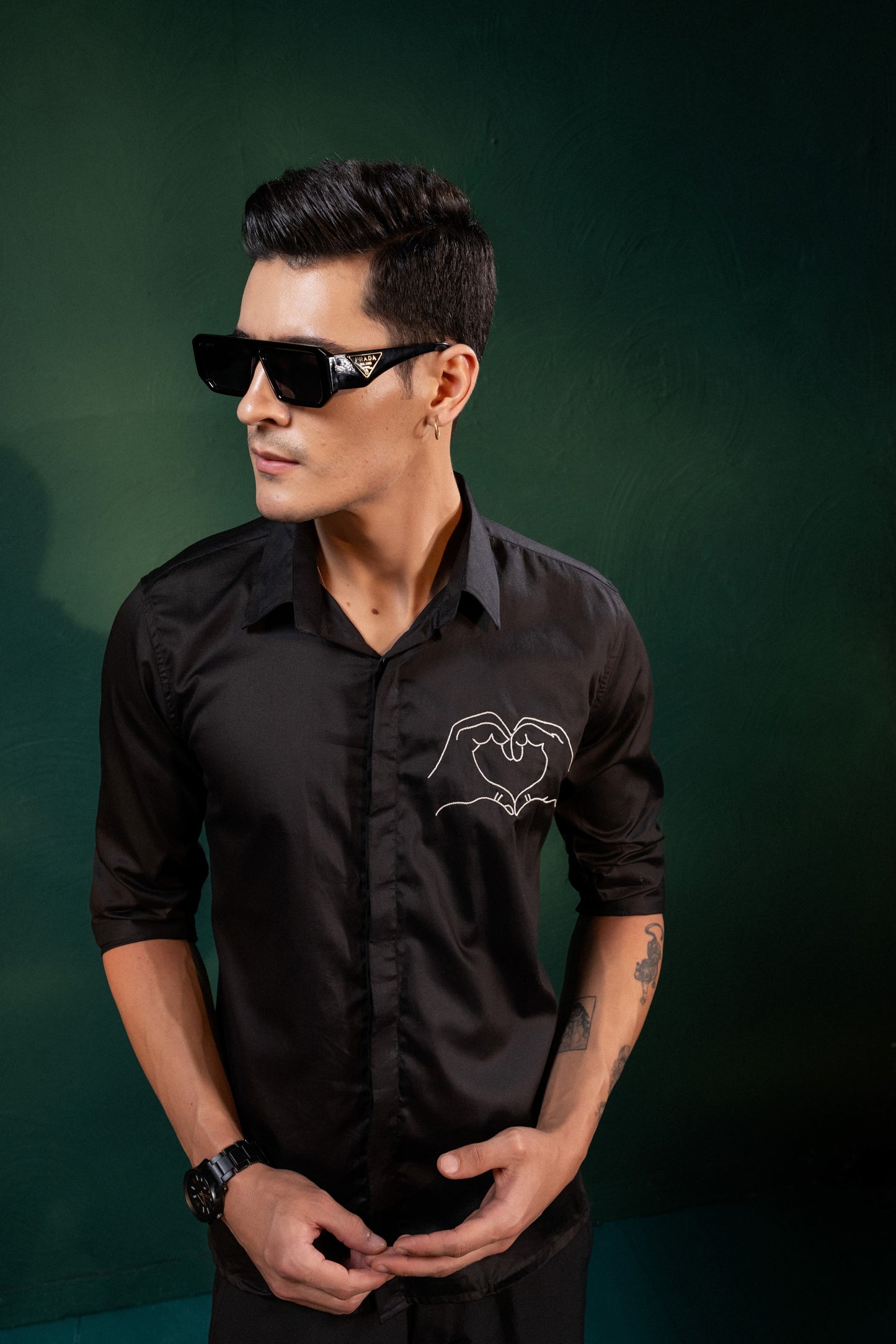 A HEART GESTURE SHOWN WITH HANDS EMBROIDERED ON A SHIRT