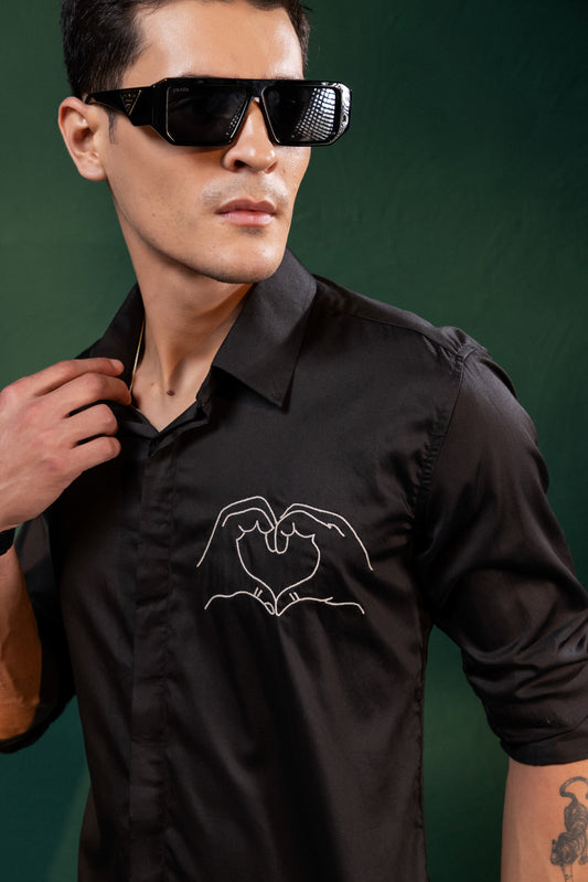 A HEART GESTURE SHOWN WITH HANDS EMBROIDERED ON A SHIRT